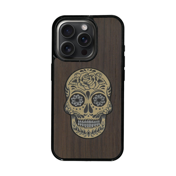 Coque de protection en bois véritable fabriquée en France pour iPhone 16 Pro + MagSafe® alliant du chêne fumé avec du métal argenté et doré représentant une tête de mort mexicaine sur le thème Dia de los Muertos