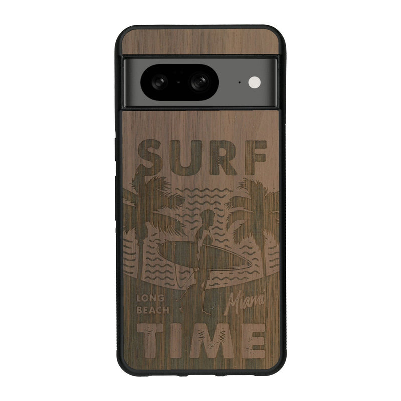 Coque de protection en bois véritable fabriquée en France pour Google Pixel 7A sur le thème chill avec un motif représentant une silouhette tenant une planche de surf sur une plage entouré de palmiers et les mots "Surf Time Long Beach Miami"