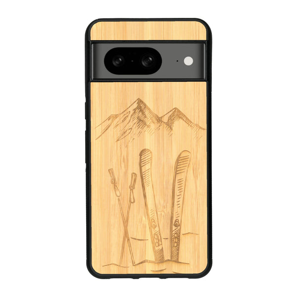 Coque de protection en bois véritable fabriquée en France pour Google Pixel 8A sur le thème de la montagne, du ski et de la neige avec un motif représentant une paire de ski plantée dans la neige avec en fond des montagnes enneigées