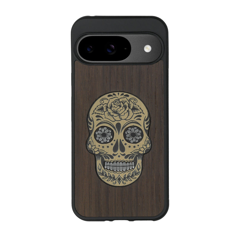 Coque de protection en bois véritable fabriquée en France pour Google Pixel 9 alliant du chêne fumé avec du métal argenté et doré représentant une tête de mort mexicaine sur le thème Dia de los Muertos