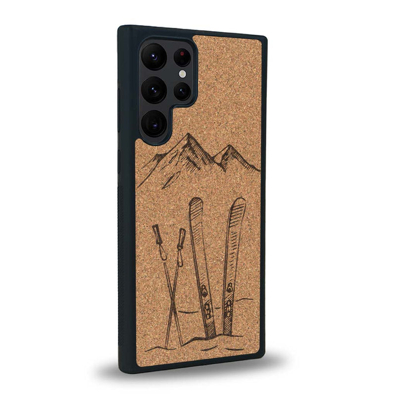 Coque de protection en bois véritable fabriquée en France pour Samsung S24 Ultra sur le thème de la montagne, du ski et de la neige avec un motif représentant une paire de ski plantée dans la neige avec en fond des montagnes enneigées