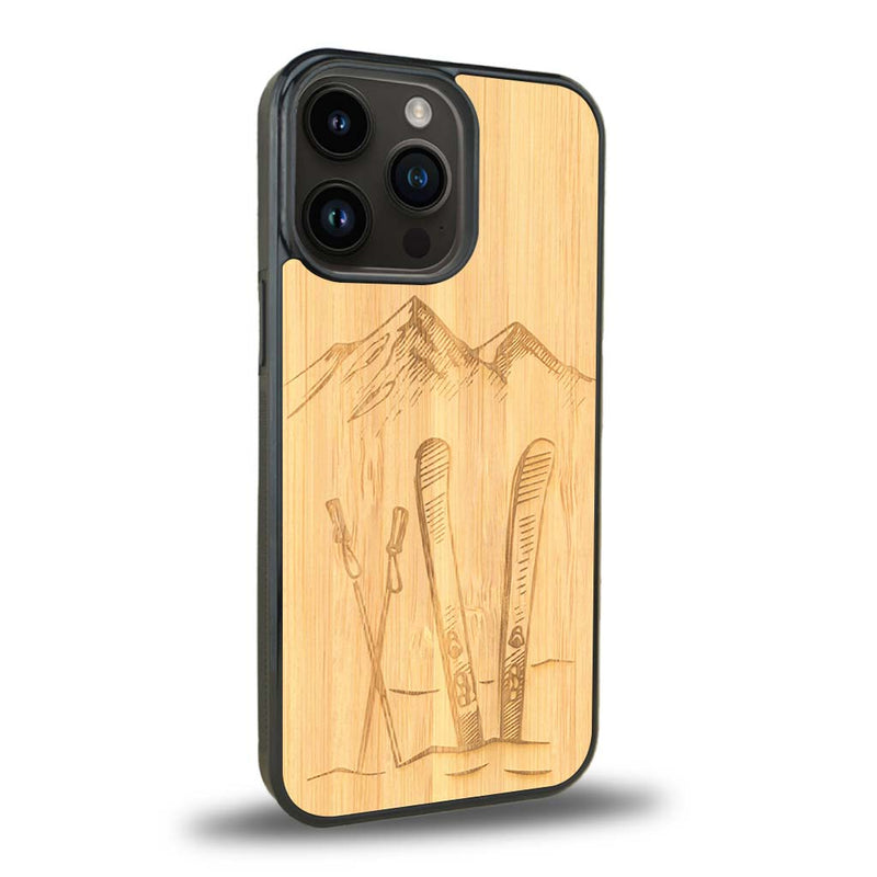 Coque de protection en bois véritable fabriquée en France pour iPhone 15 Pro Max sur le thème de la montagne, du ski et de la neige avec un motif représentant une paire de ski plantée dans la neige avec en fond des montagnes enneigées