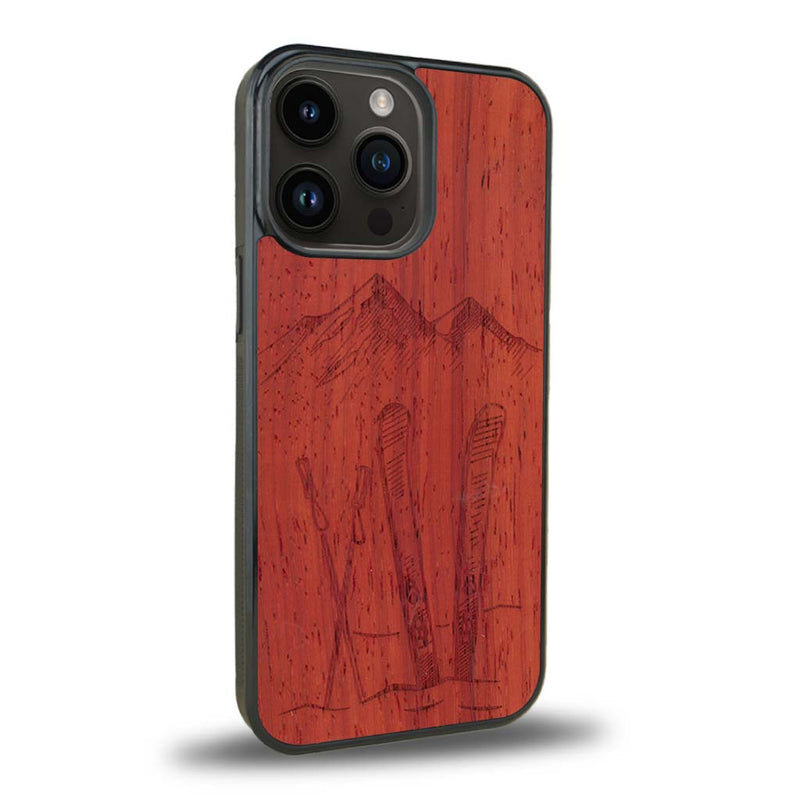 Coque de protection en bois véritable fabriquée en France pour iPhone 15 Pro Max sur le thème de la montagne, du ski et de la neige avec un motif représentant une paire de ski plantée dans la neige avec en fond des montagnes enneigées