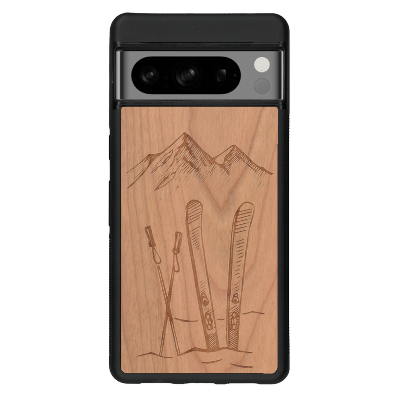 Coque de protection en bois véritable fabriquée en France pour Google Pixel 7pro sur le thème de la montagne, du ski et de la neige avec un motif représentant une paire de ski plantée dans la neige avec en fond des montagnes enneigées