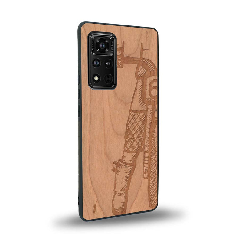 Coque de protection en bois véritable fabriquée en France pour Honor V40 représentant une vue de face d'une femme sur une moto vintage dessinée à la main par l'artiste Maud Dabs