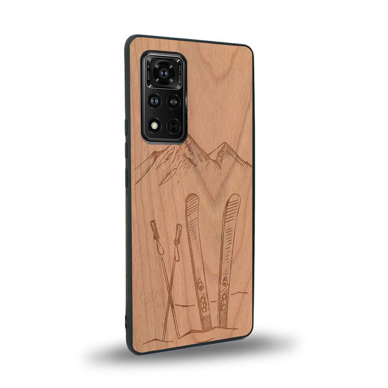 Coque de protection en bois véritable fabriquée en France pour Honor V40 sur le thème de la montagne, du ski et de la neige avec un motif représentant une paire de ski plantée dans la neige avec en fond des montagnes enneigées