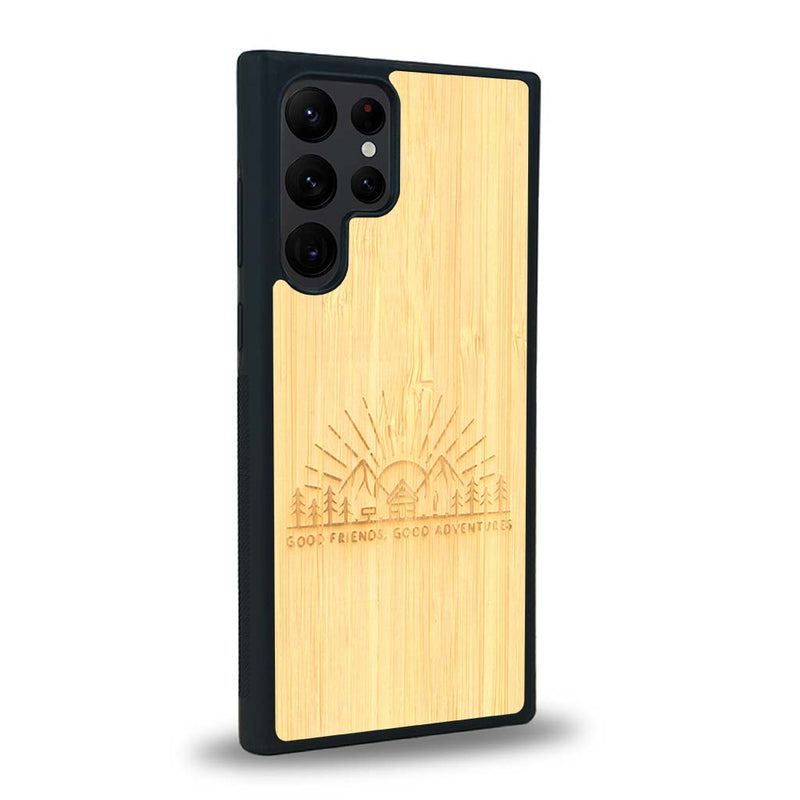 Coque de protection en bois véritable fabriquée en France pour Samsung S23 Ultra sur le thème chill et nature avec un motif représentant un levé de soleil sur un paysage de montagne avec des sapins et un chalet et la phrase "Good friends, good adventure"