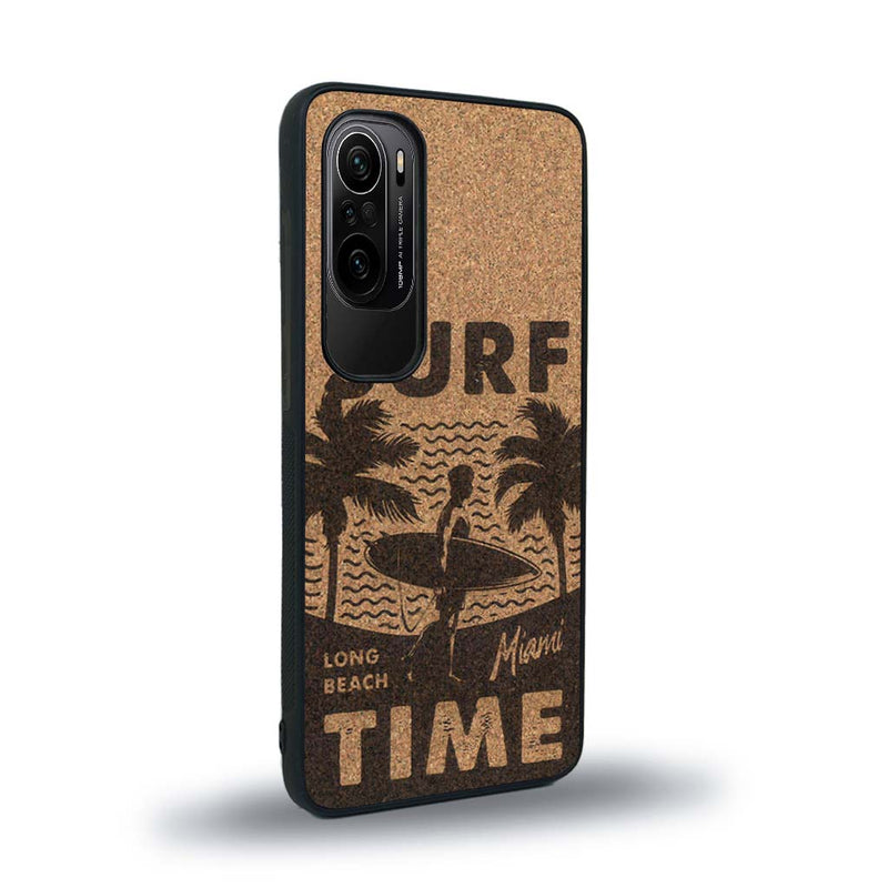 Coque de protection en bois véritable fabriquée en France pour Xiaomi Mi 11i sur le thème chill avec un motif représentant une silouhette tenant une planche de surf sur une plage entouré de palmiers et les mots "Surf Time Long Beach Miami"