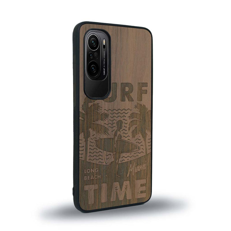 Coque de protection en bois véritable fabriquée en France pour Xiaomi Mi 11i sur le thème chill avec un motif représentant une silouhette tenant une planche de surf sur une plage entouré de palmiers et les mots "Surf Time Long Beach Miami"