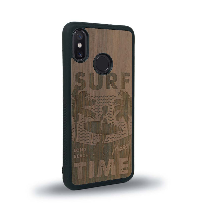 Coque de protection en bois véritable fabriquée en France pour Xiaomi Mi 8 sur le thème chill avec un motif représentant une silouhette tenant une planche de surf sur une plage entouré de palmiers et les mots "Surf Time Long Beach Miami"