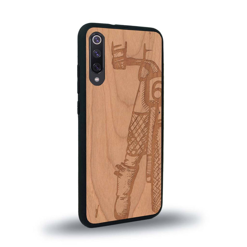 Coque de protection en bois véritable fabriquée en France pour Xiaomi Mi 9SE représentant une vue de face d'une femme sur une moto vintage dessinée à la main par l'artiste Maud Dabs