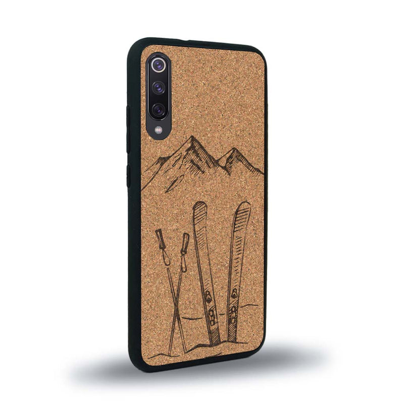 Coque de protection en bois véritable fabriquée en France pour Xiaomi Mi 9SE sur le thème de la montagne, du ski et de la neige avec un motif représentant une paire de ski plantée dans la neige avec en fond des montagnes enneigées