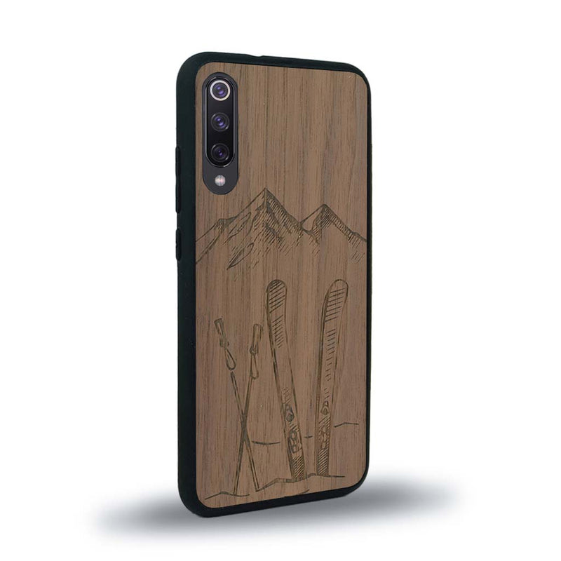 Coque de protection en bois véritable fabriquée en France pour Xiaomi Mi 9SE sur le thème de la montagne, du ski et de la neige avec un motif représentant une paire de ski plantée dans la neige avec en fond des montagnes enneigées